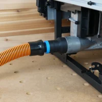 Black 1-1/4" hose adapter with blue ring joining an orange vac hose to a Milwaukee M18 table saw dust port