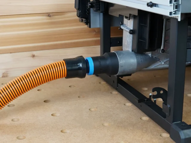 Black 1-1/4" hose adapter with blue ring joining an orange vac hose to a Milwaukee M18 table saw dust port