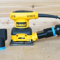 Black ToolCurve 1-1/4 inch hose adapter with blue ring beside a DeWalt palm sander with hose attached