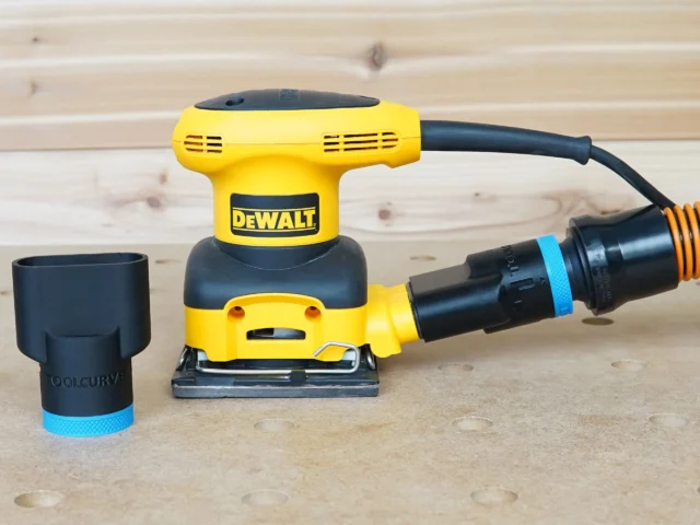 Black ToolCurve 1-1/4 inch hose adapter with blue ring beside a DeWalt palm sander with hose attached