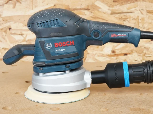 Black ToolCurve 1-7/8 inch hose adapter with blue band joining a vacuum hose to a Bosch ROS65VC sander dust port