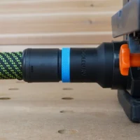 Black hose adapter with blue band and orange quick-release collar attached to green-and-yellow braided hose on Wen belt and disc sander