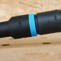 ToolCurve hose adapter with blue band attached to Bosch GEX34-6N sander dust port, shown at angle on wood surface