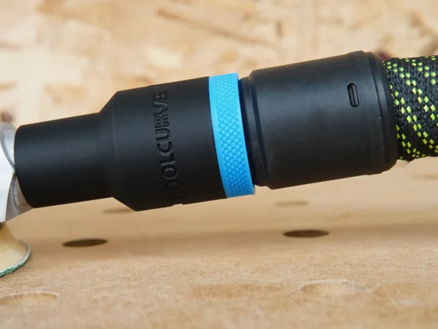 ToolCurve hose adapter with blue band attached to Bosch GEX34-6N sander dust port, shown at angle on wood surface
