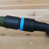 Black hose adapter with blue band attached to green-and-black braided hose, connected to Dewalt disc sander dust port on wooden workbench