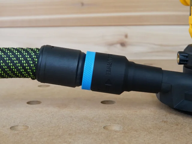Black hose adapter with blue band attached to green-and-black braided hose, connected to Dewalt disc sander dust port on wooden workbench