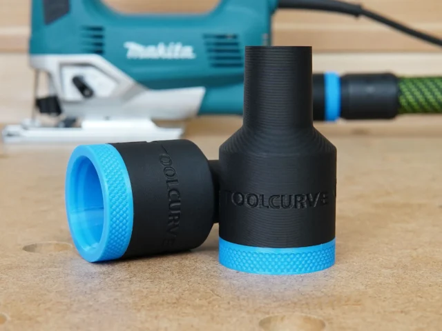 Black and blue plastic hose adapter with "ToolCurve" and "Makita" text molded into the body, shown alongside its blue threaded ring component on a wooden surface with a Makita jig saw blurred in the background