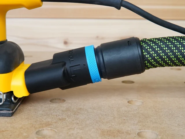 Black hose adapter with blue band attached to Dewalt palm sander dust port, connected to green braided hose