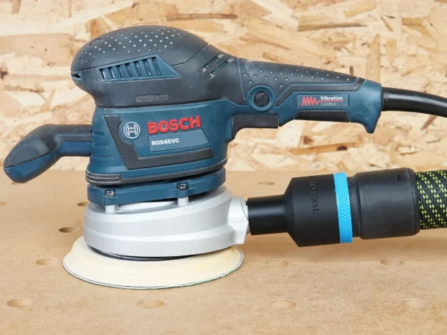 Black 36mm hose adapter with blue band joining an extractor hose to a Bosch ROS65VC sander dust port