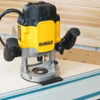 DeWalt DWE625 plunge router mounted on a guide rail adapter, sitting on a Makita track rail over plywood