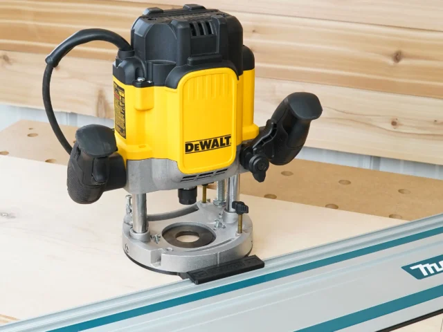DeWalt DWE625 plunge router mounted on a guide rail adapter, sitting on a Makita track rail over plywood