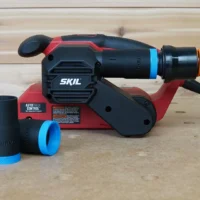 Black 1-1/4 inch hose adapter with blue ring installed on a SKIL belt sander port, two spare adapters beside it