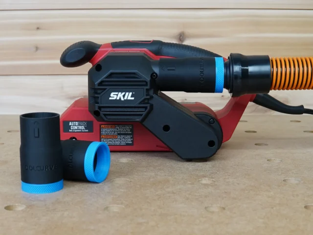 Black 1-1/4 inch hose adapter with blue ring installed on a SKIL belt sander port, two spare adapters beside it