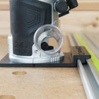 Kobalt 24v router guide rail adapter mounted on a router, attached to a Festool guide rail on wooden workbench