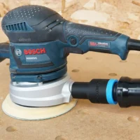 Black ToolCurve 1-1/4 inch hose adapter linking an orange extractor hose to a Bosch ROS65VC sander dust port