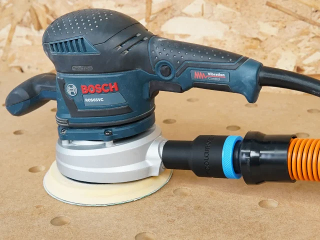 Black ToolCurve 1-1/4 inch hose adapter linking an orange extractor hose to a Bosch ROS65VC sander dust port