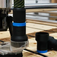 Black hose adapter with blue band attached to Onefinity CNC dust boot, with matching spare adapter beside it on wooden workbench