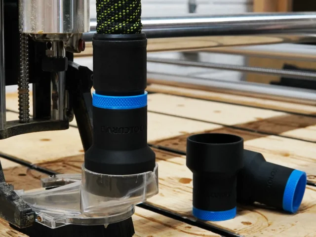 Black hose adapter with blue band attached to Onefinity CNC dust boot, with matching spare adapter beside it on wooden workbench