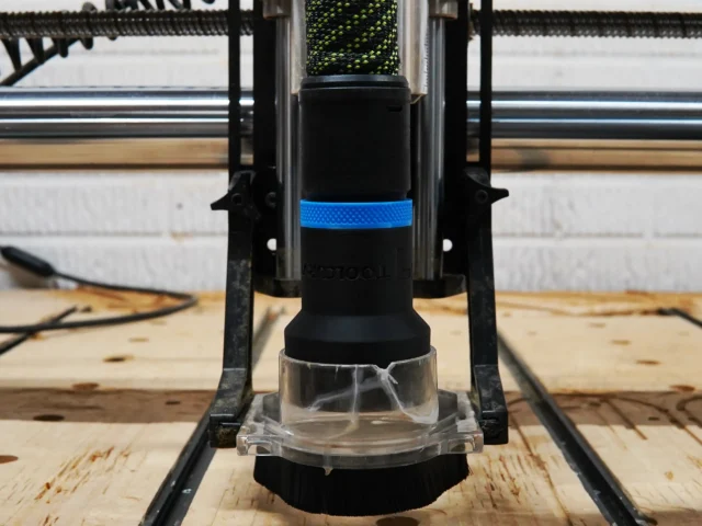 Hose adapter mounted on Onefinity CNC dust boot, showing clear base and black body with blue band, attached to workshop track saw