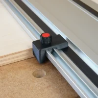 Black plastic drop stop with red knurled knob attached to a Milwaukee track saw guide rail above a workbench