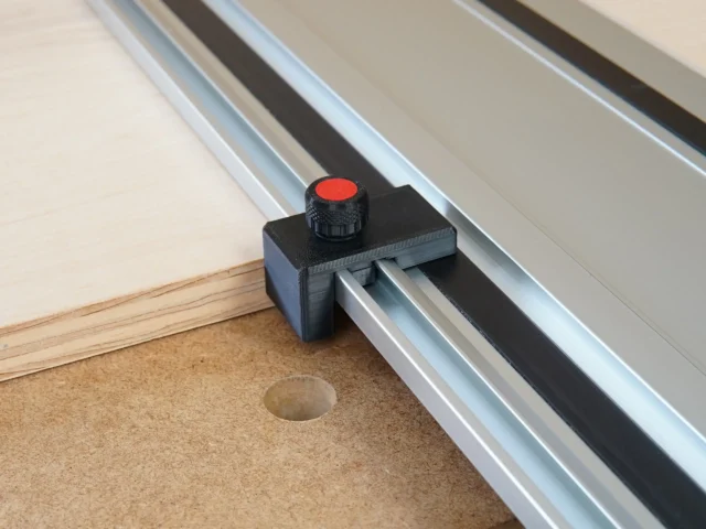 Black plastic drop stop with red knurled knob attached to a Milwaukee track saw guide rail above a workbench