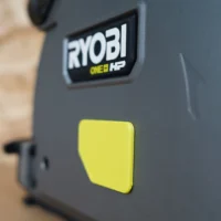 Yellow snap-on dust cover attached to Ryobi ONE+ HP track saw, showing low-profile design and branded nameplate
