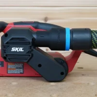 Black ToolCurve 36mm hose adapter with blue ring fitted to the dust port of a red SKIL belt sander