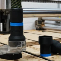Black plastic hose adapter with blue band installed on Onefinity CNC dust boot, clear collar visible at base, spare adapter shown beside it