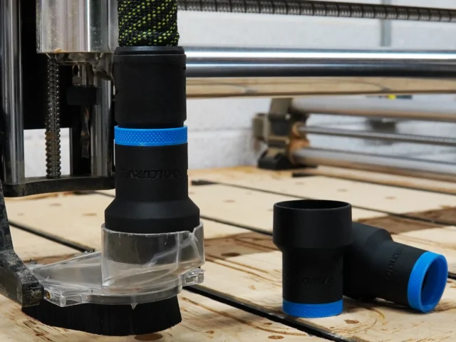 Black plastic hose adapter with blue band installed on Onefinity CNC dust boot, clear collar visible at base, spare adapter shown beside it