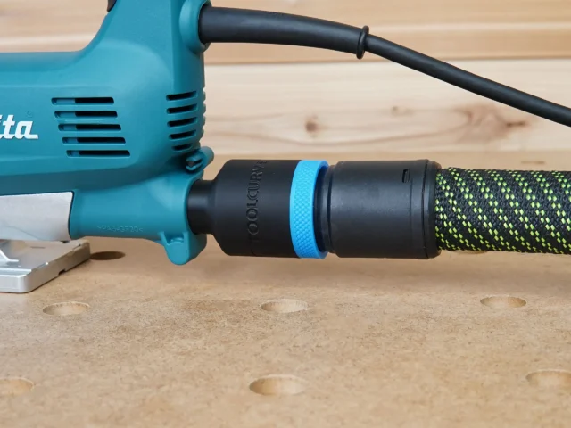 Black hose adapter with blue band attached to turquoise Makita jig saw, connected to green and black braided hose