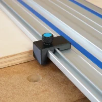 Black plastic drop stop mounted on Kreg track saw rail with blue knurled knob, shown against wooden workpiece edge