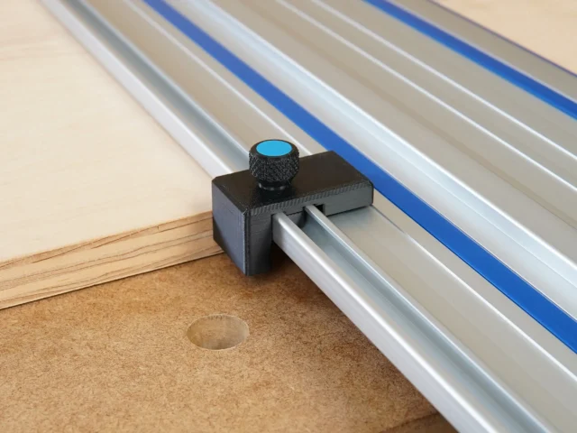 Black plastic drop stop mounted on Kreg track saw rail with blue knurled knob, shown against wooden workpiece edge