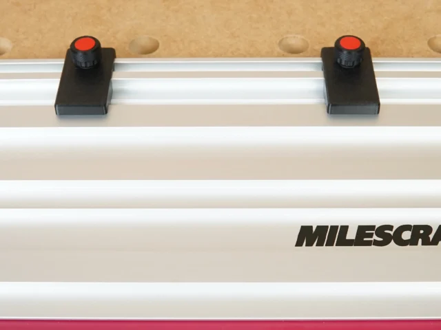 Two black limit stops with red knobs mounted on a Milescraft guide rail, spaced apart for repeatable cuts