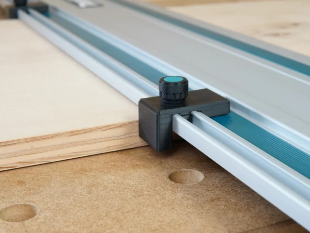 Black plastic drop stop mounted on Makita track saw rail with turquoise knurled knob, positioned at workpiece edge on cork base