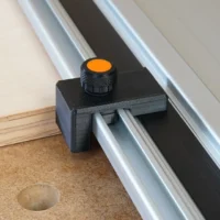 Black drop stop mounted on Powertec track saw guide rail with orange knurled knob, positioned above cork workbench