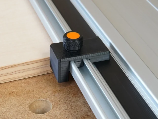 Black drop stop mounted on Powertec track saw guide rail with orange knurled knob, positioned above cork workbench