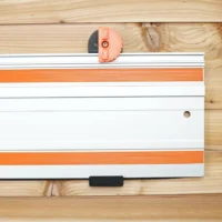 Orange 3D-printed wall mount clipped onto white aluminum Wen track saw rail, shown mounted on wooden wall