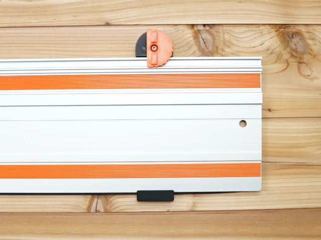 Orange 3D-printed wall mount clipped onto white aluminum Wen track saw rail, shown mounted on wooden wall