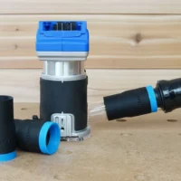 Black 1-1/4 inch hose adapter with blue collar joined to an orange vacuum hose beside a Kobalt 24v router, second adapter on bench