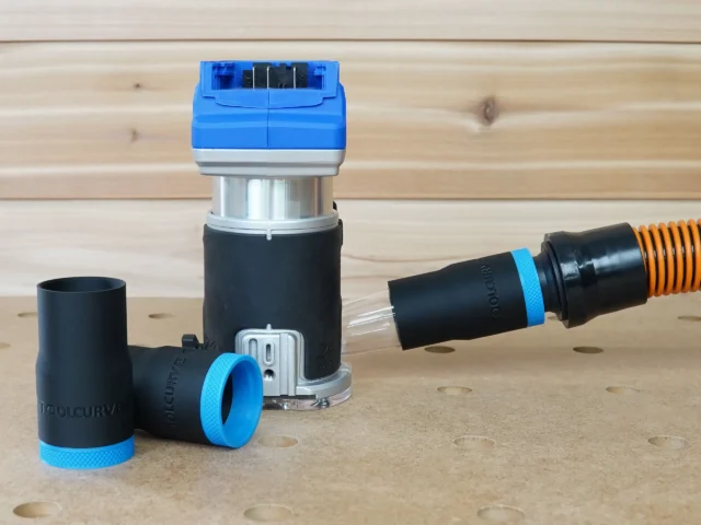 Black 1-1/4 inch hose adapter with blue collar joined to an orange vacuum hose beside a Kobalt 24v router, second adapter on bench