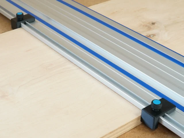 Two black drop stops with blue knobs mounted on opposite ends of a Kreg track saw guide rail, positioned at the rail edges on a wooden workpiece