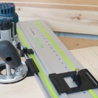 Bosch Colt plunge base router mounted to Festool LR 32 guide rail with black adapter plate and spring-loaded positioning knob installed