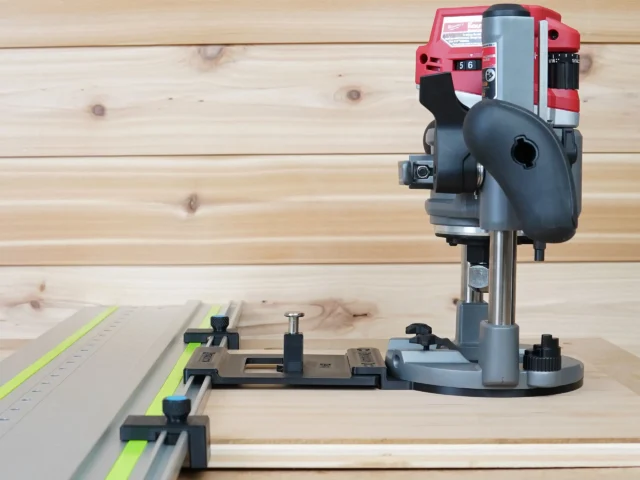 Milwaukee M18 2 1/4" HP router mounted on LR 32 plunge base with rail adapter, positioned over a Festool-style track with guide stops for hole drilling