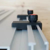 Black limit stop with knurled knob mounted on silver Milescraft guide rail, shown at angle on wooden workbench