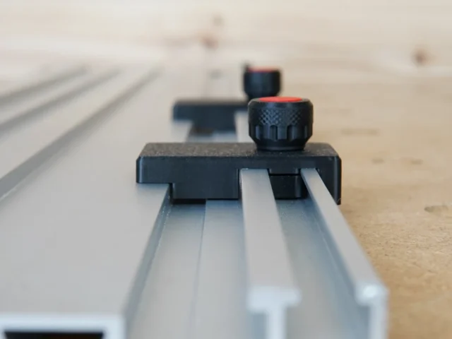 Black limit stop with knurled knob mounted on silver Milescraft guide rail, shown at angle on wooden workbench