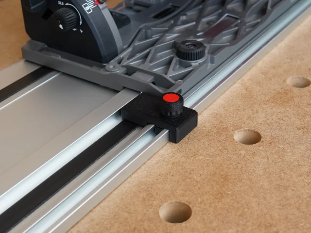 Black limit stop with red knob mounted on Milwaukee guide rail, shown attached to track saw fence on cork workbench