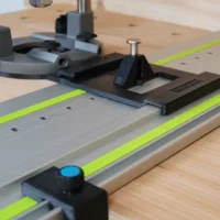 Milwaukee M18 router mounted on Festool-style guide rail with black LR 32 plunge base, stop block, and spring-loaded knob positioned on wood
