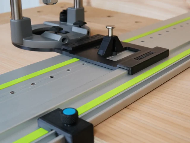 Milwaukee M18 router mounted on Festool-style guide rail with black LR 32 plunge base, stop block, and spring-loaded knob positioned on wood