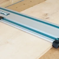 Two black drop stops mounted on a Makita track saw guide rail, positioned at each end to register against workpiece edges