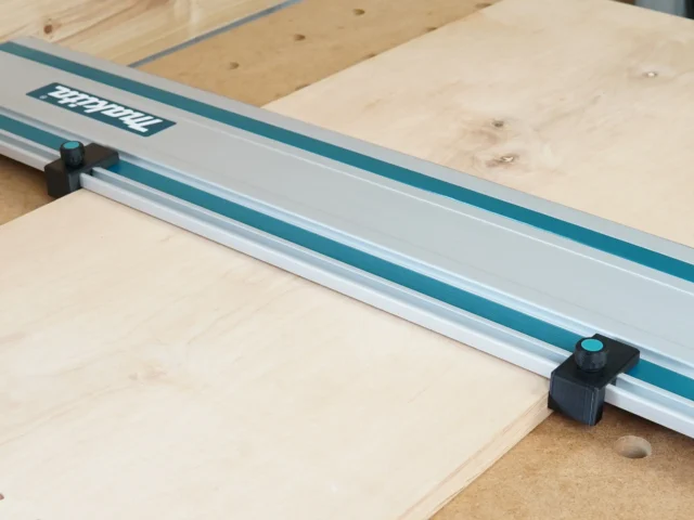 Two black drop stops mounted on a Makita track saw guide rail, positioned at each end to register against workpiece edges